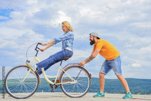 Girl cycling while man support her. Man helps keep balance ride bike. Cycling service. Service and assistance. Mechanic helps maintain bicycle. Supportive service. Woman rides bicycle sky background