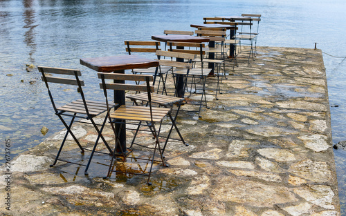 Empty wooden chairs around tables outside a bar by the sea