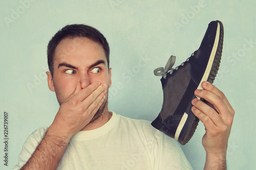 A man pinches his nostrils closed over the odor given off from the athletic shoe he is holding