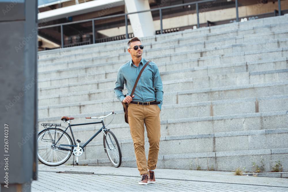 handsome middle aged businessman in sunglasses walking on street, bicycle on background handsome middle aged businessman in sunglasses walking on street, bicycle on background