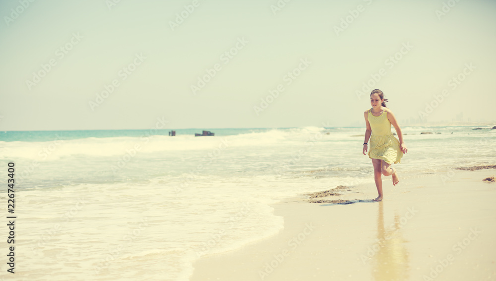 12 years old girl teen girl in yellow dress walking on seaside. Summer vacation