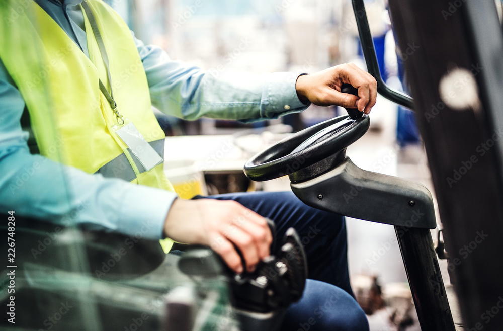 Unrecognizable industrial man engineer sitting in a forklift in a factory. Unrecognizable industrial man engineer sitting in a forklift in a factory.