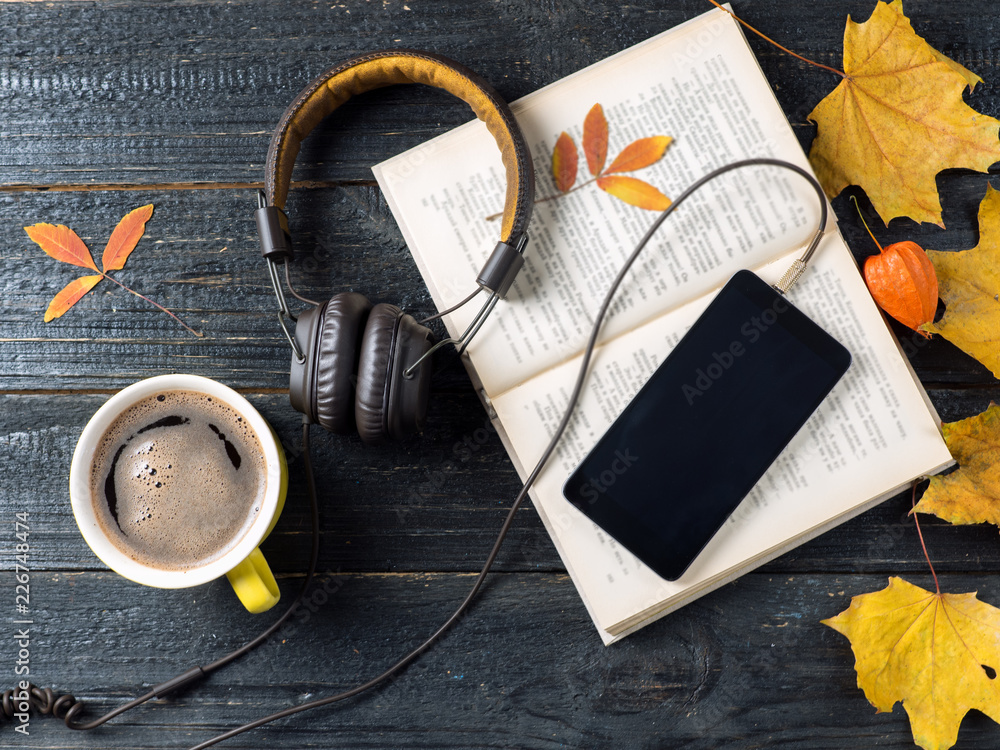 Fototapeta premium Autumn leaves, coffee, telephone with headphones and audio book concept, modern electronic library