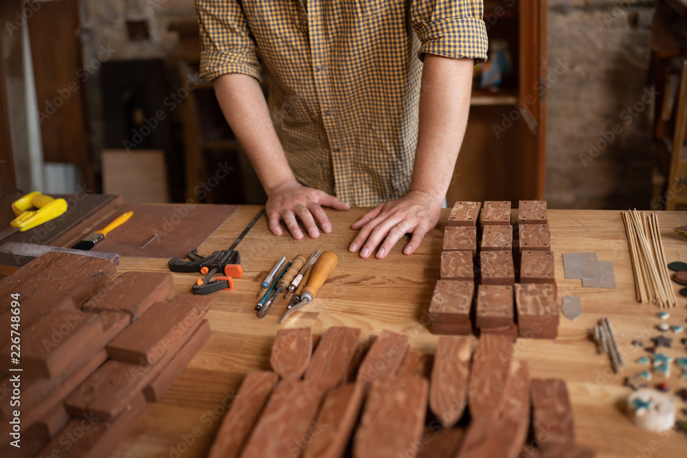 Close-up view of a wood carpenter's hands. Joiner's flanel. Instruments for wood carving and wooden bricks are laying on the table. Close-up view of a wood carpenter's hands. Joiner's flanel. Instruments for wood carving and wooden bricks are laying on the table.