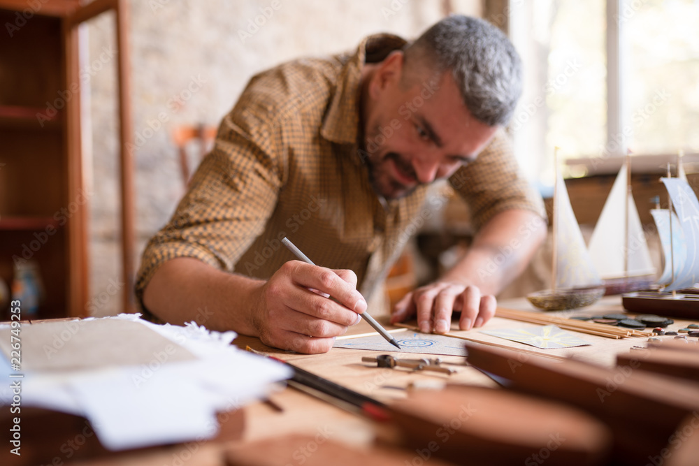 Blurred joiner during his work on sketching his project. Close-up view of a pencil and a protractor. Blurred joiner during his work on sketching his project. Close-up view of a pencil and a protractor.