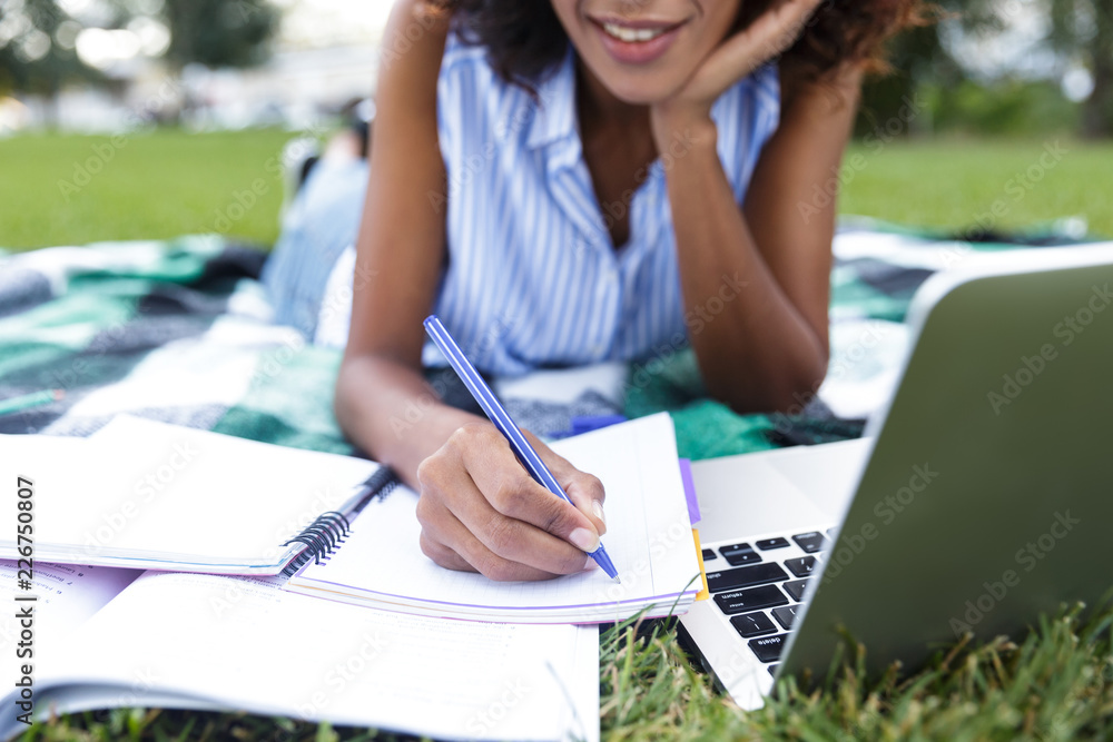Obraz premium Happy smiling young girl doing homework using laptop outdoors in park.