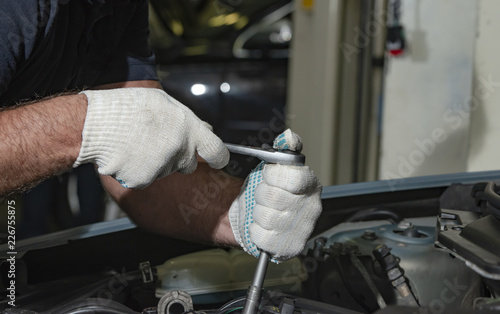 Close up hands in white textile gloves of mechanic doing car service and maintenance in a car repair garage