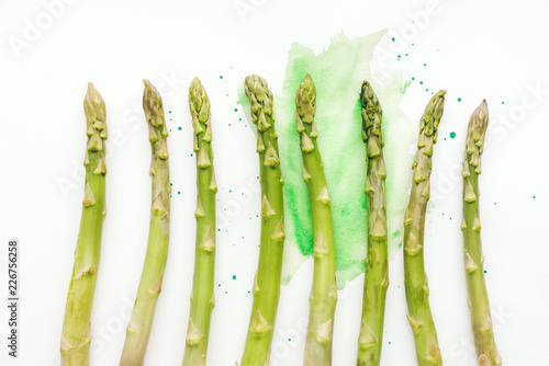 top view of row of ripe asparagus stems on white surface with green watercolor strokes