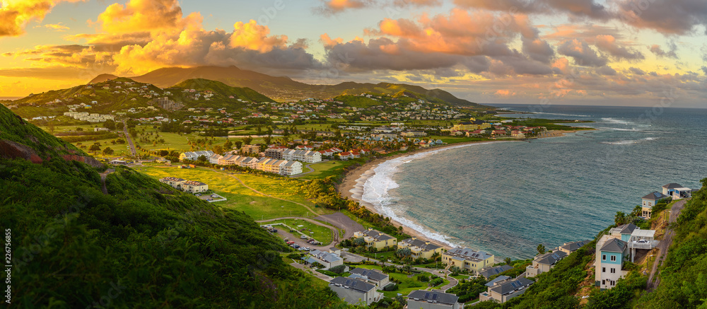 Panorama of Saint Kitts and its capital Basseterre during sunset, beautiful green mountains and a beach in paradise caribbean island with amazing green and orange colors. Saint kitts and nevis - obrazy, fototapety, plakaty 