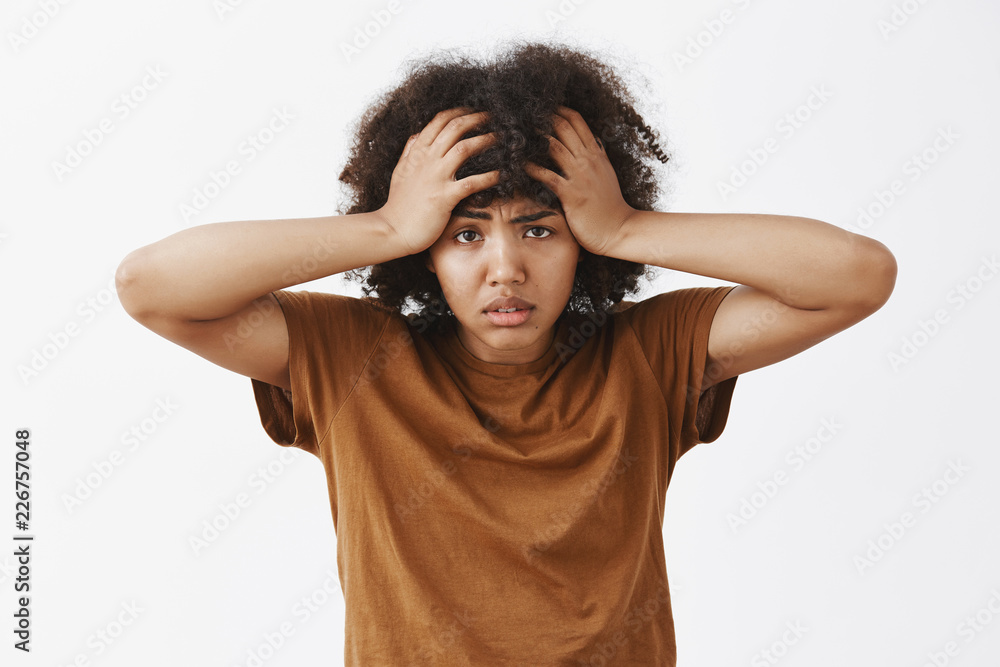 Waist-up shot of bothered and tired depressed african american woman with afro hairstyle feeling annoyed and exhausted with louds of troubles on head frowning holding hands on hair Waist-up shot of bothered and tired depressed african american woman with afro hairstyle feeling annoyed and exhausted with louds of troubles on head frowning holding hands on hair