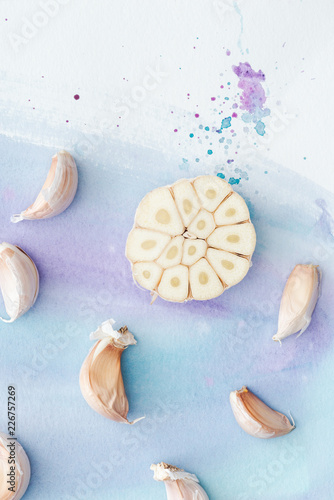 top view of sliced garlic on white surface with purple watercolor strokes