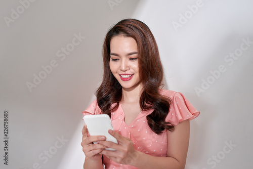 Portrait of an attractive young asian woman using mobile phone while standing with copy space over gray background