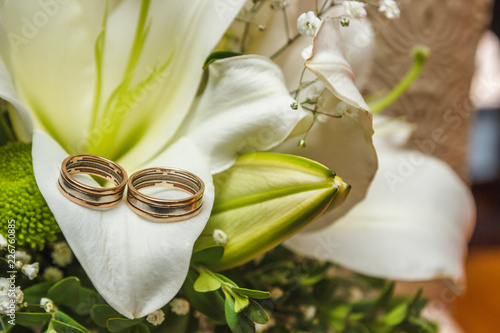 Photo image of a classic wedding gold rings of the bride and groom on a white table, with a beautiful wedding bouquet of flowers of the bride