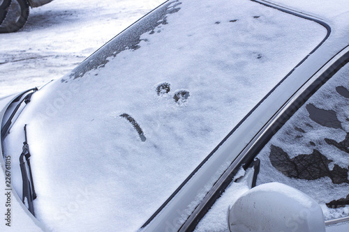 The car covered with snow with a evil face on the glass. Winter landscape.