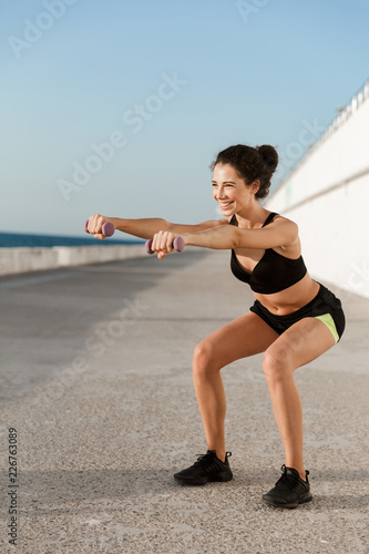 Young sports woman make exercises with dumbbells outdoors on the beach.