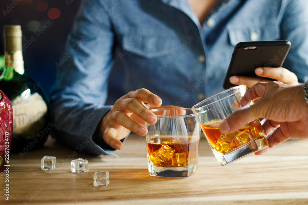 Close-up of two men clink glasses of whiskey drink alcoholic beverage together at bar counter in pub Close-up of two men clink glasses of whiskey drink alcoholic beverage together at bar counter in pub