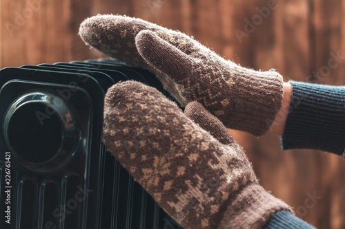 Women's hands in Christmas, warm, winter mittens on the heater. Keep warm in the winter, cold evenings