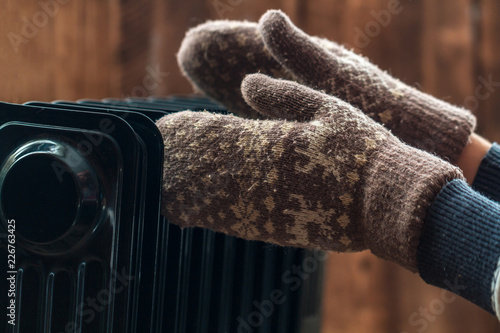 Women's hands in Christmas, warm, winter mittens on the heater. Keep warm in the winter, cold evenings