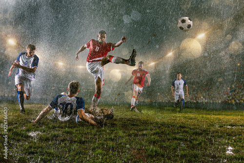 Soccer players performs an action play on a professional night rain stadium. Dirty players in rain drops scores a goal. Grass in the stadium wet from the rain