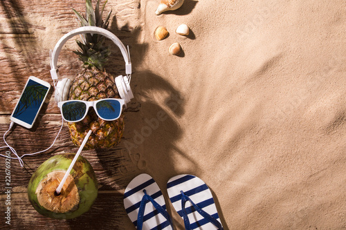 Ripe pineapple with sunglasses and headphones on beach sand