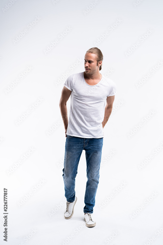 Full length of a cute young man in jeans and t-shirt looking at the camera, against white background. Full length of a cute young man in jeans and t-shirt looking at the camera, against white background.