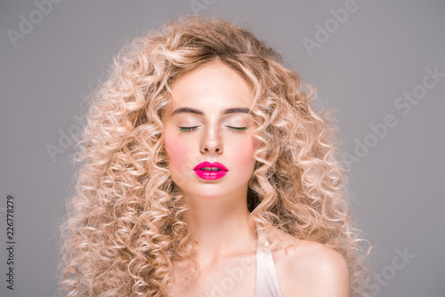 beautiful young woman with long curly hair standing with closed eyes isolated on grey