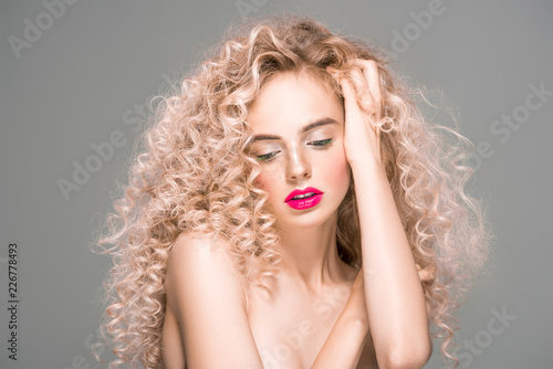 portrait of beautiful naked young woman with long curly hair looking down isolated on grey