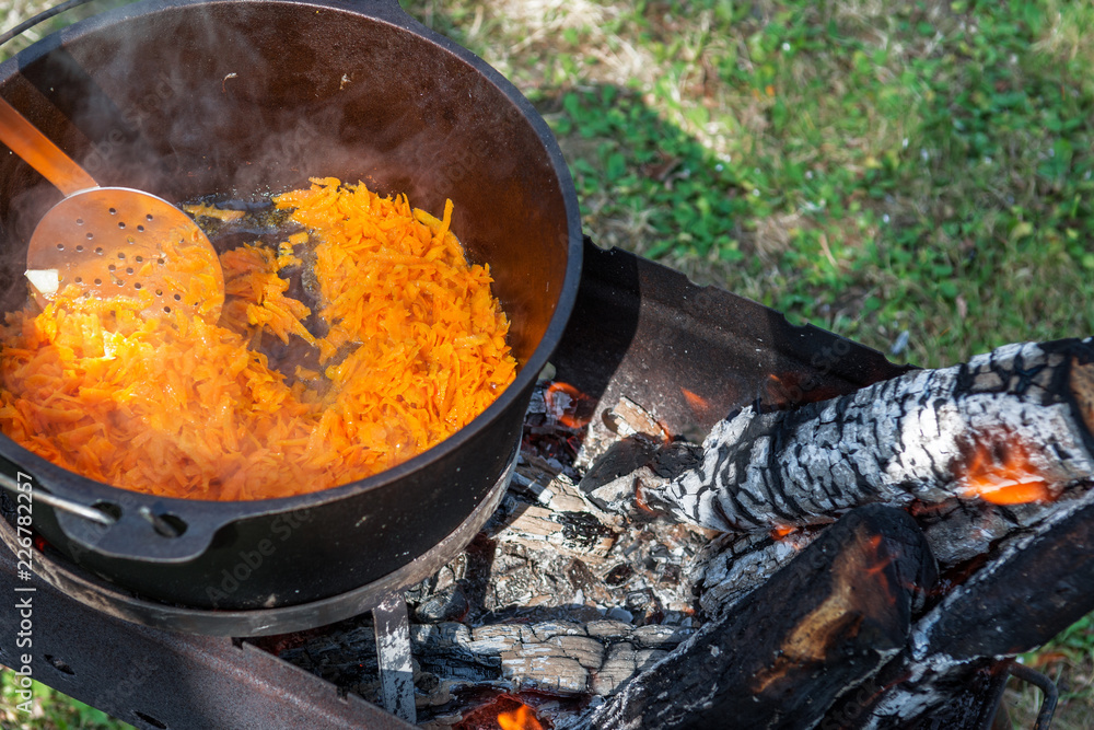 Carrots are cooking in the pot on the fire for rice pilau. Camping in the nature and preparing food concept Carrots are cooking in the pot on the fire for rice pilau. Camping in the nature and preparing food concept