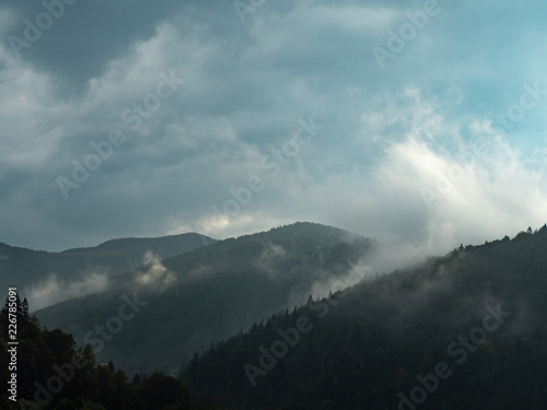 Dense rainy clouds above the hillsides at summer. Carpathians mountains in august, west Ukraine. Wood of green fir and pine trees. Wild nature landscape. Rainy day. Blurred background © eriksvoboda