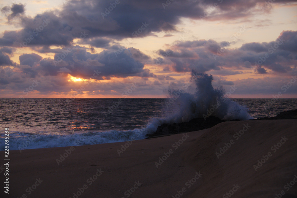 Closeup of wave crashing on rocks, against beautiful sunset