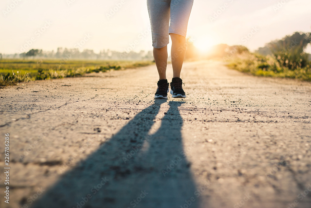 Young sporty fitness woman trail running on the rural road in summer with sunset background Young sporty fitness woman trail running on the rural road in summer with sunset background
