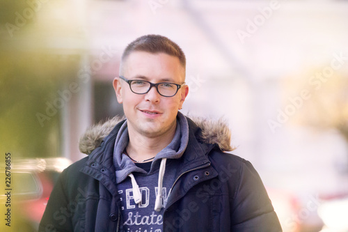 handsome cheerful short-cut man in black glasses in a black jacket walks through the autumn streets of the city