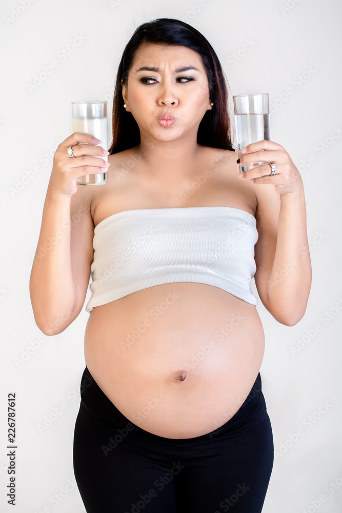 Close-up of confused pregnant woman holding milk and water glass isolated over white background Close-up of confused pregnant woman holding milk and water glass isolated over white background