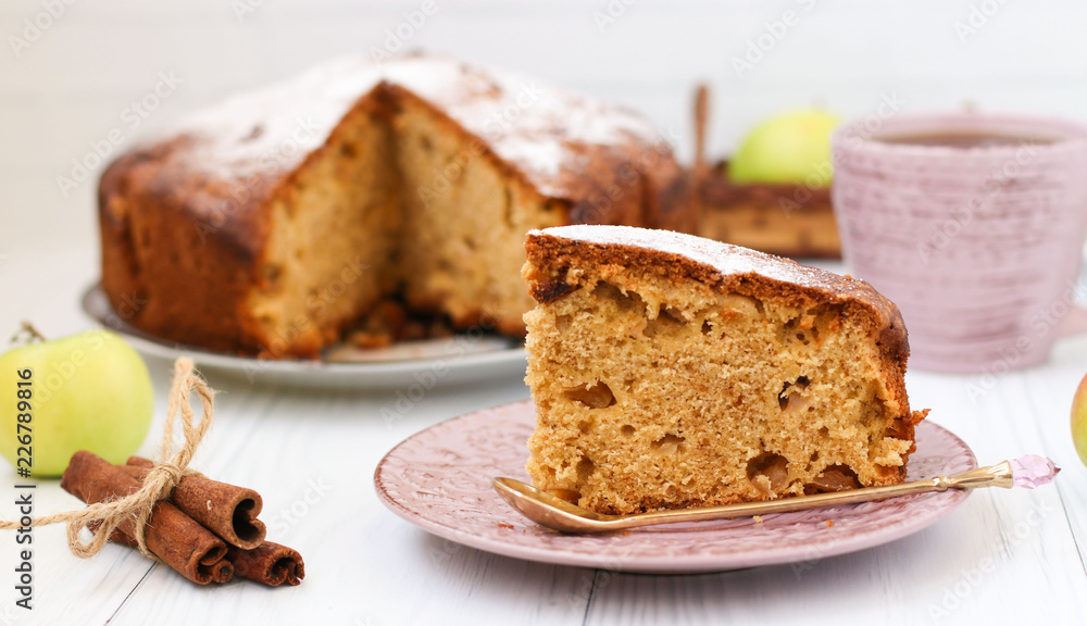 Pie with apples, cinnamon and ginger on a white background. A piece of cake in the foreground. On the photo, apples, cinnamon sticks and a cup of coffee. Pie with apples, cinnamon and ginger on a white background. A piece of cake in the foreground. On the photo, apples, cinnamon sticks and a cup of coffee.