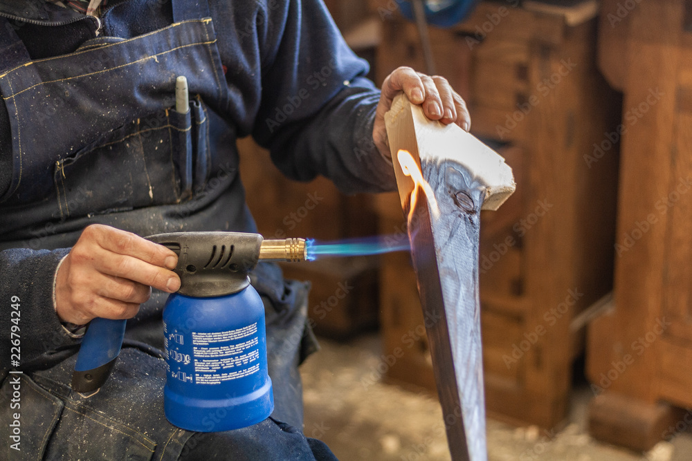 Detailed shot of a professional carpenter, in his laboratory, treating and processing wooden elements with fire. Gas burner, pistol, natural texture, organic construction. Burnt furniture with black f Detailed shot of a professional carpenter, in his laboratory, treating and processing wooden elements with fire. Gas burner, pistol, natural texture, organic construction. Burnt furniture with black f