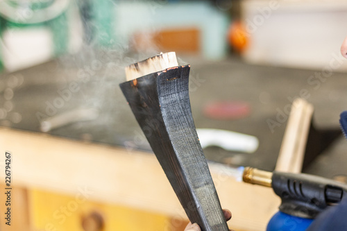 Detailed shot of a professional carpenter, in his laboratory, treating and processing wooden elements with fire. Gas burner, pistol, natural texture, organic construction. Burnt furniture with black f