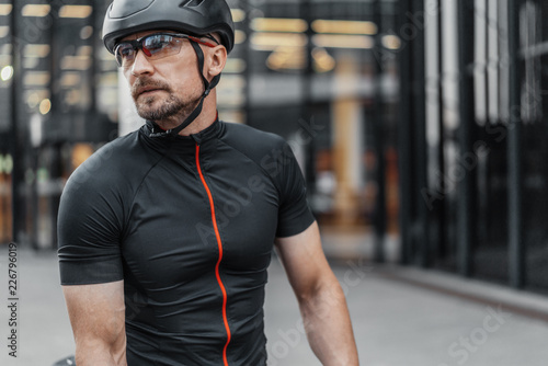 Sportsman riding bike next to glass facades of skyscrapers. Urban background.
