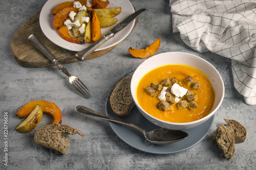 Close up of served fresh hokkaido pumpkin creamy soup with pieces of bread, baked pumkpin, potatoes and goat cheese on rustic background photo