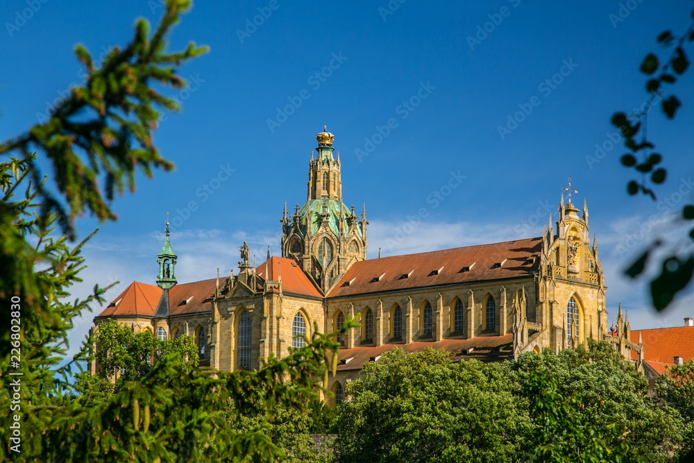 Obraz premium Monumental monastery of Benedictines in Kladruby, Czech Republic, Europe from 12th century standing on hill, includes church of All Saints, red roof, green foreground, sunny summer day, blue sky