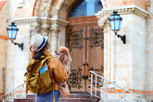 Woman traveler with backpack holding dog examines architectural monument . Concept of travel.