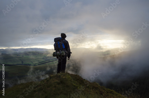 Hiker Watching the Sunset through the Clouds over the Landscape