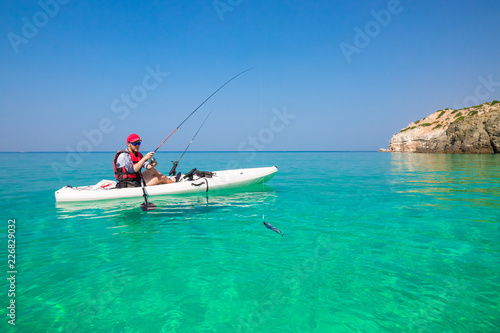 Fishing kayak in the sea on the islands. Man fisherman catch a fish with rod in the boat. Leisure activities on the water.