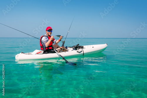 Man on a fishing kayak shows catch fish. Leisure activities on the sea. Fisherman on the islands.