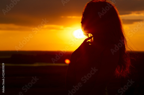 silhouette of a beautiful girl at sunset in a field, face profile of young woman enjoying nature