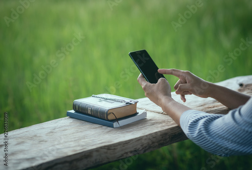 Woman sitting hands touch on a smartphone display and Bible concept of religion to the holy scripture.