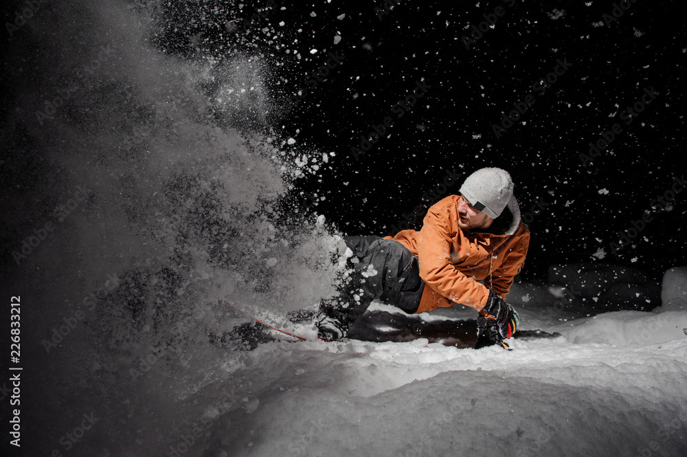 Snowboarder in orange jacket riding on a snowy hill at night Snowboarder in orange jacket riding on a snowy hill at night