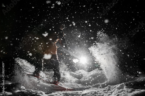 Snowboarder riding on a background of headlight and falling snow