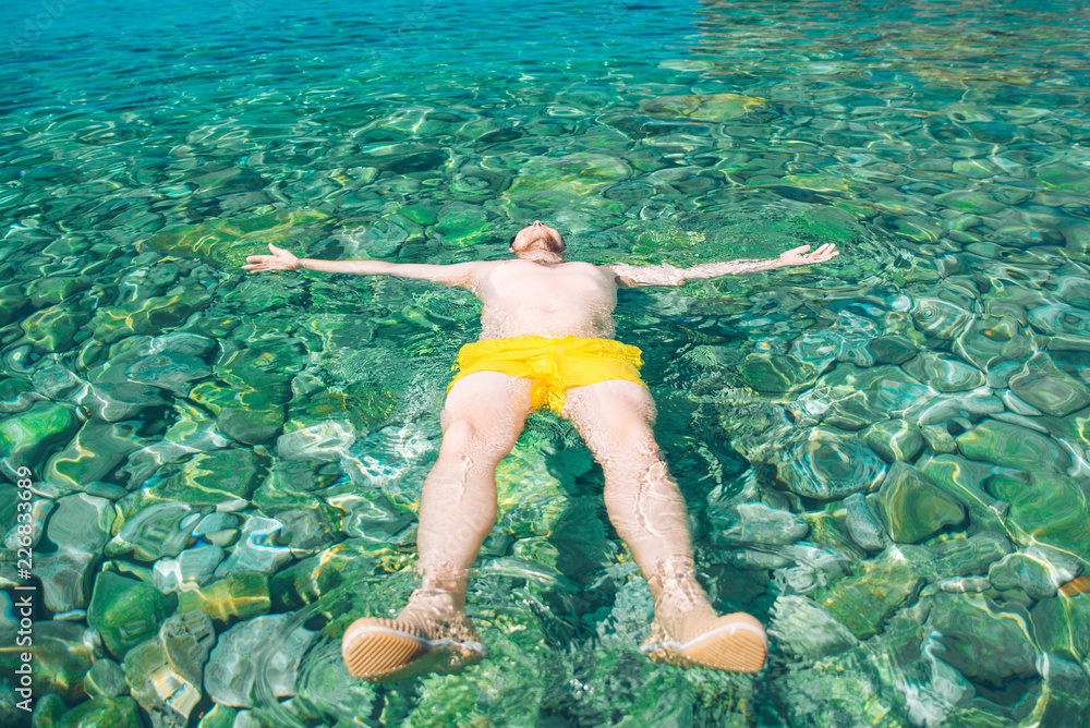 man laying at back in transparent clear water with rocky bottom