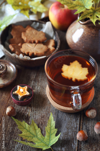 Autumn mood: cinnamon cookies in form of maple leaves, tea, red apple and yellow leaves
