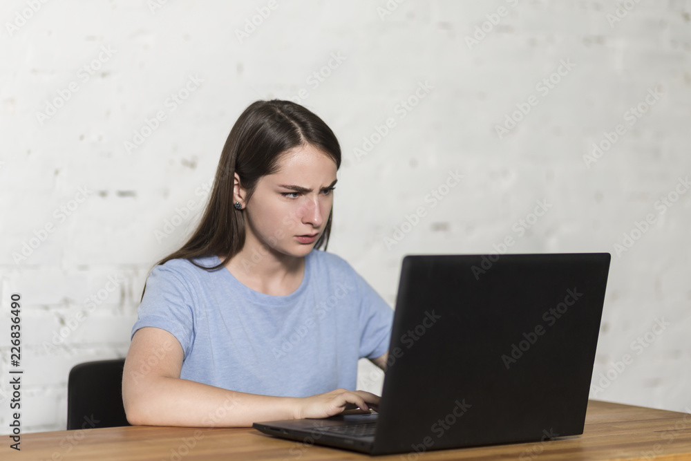Outraged girl typing on a laptop, sitting at the table. Outraged girl typing on a laptop, sitting at the table.